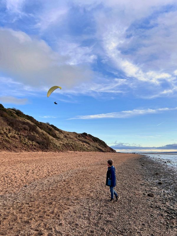 Little boy on Wirral beach, Thurstaston watching a paraglider in the blue sky above the cliff. Little boy on Wirral beach, Thurstaston watching a paraglider in the blue sky above the cliff.